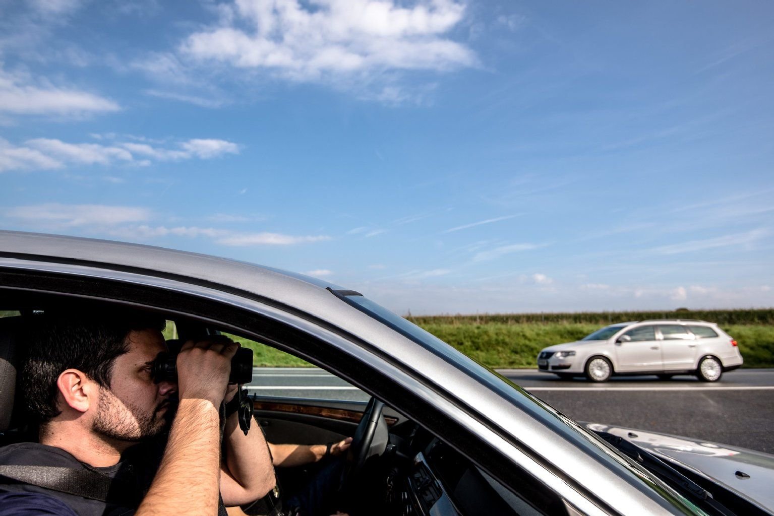 Ein Bundespolizist hält mit einem Fernglas auf einer Autobahn Ausschau nach Schleuser-Fahrzeugen.