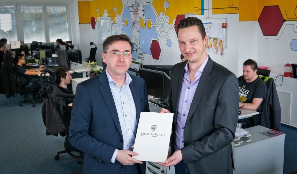 Staatssekretär Thomas Wünsch (links) überreicht einen Förderbescheid an Mathias Dögel.