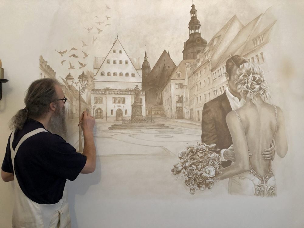 Mario Rübsam bei den letzten Pinselstrichen an seinem Kunstwerk. Das Motiv ist eine Ansicht des Eisleber Marktplatzes.