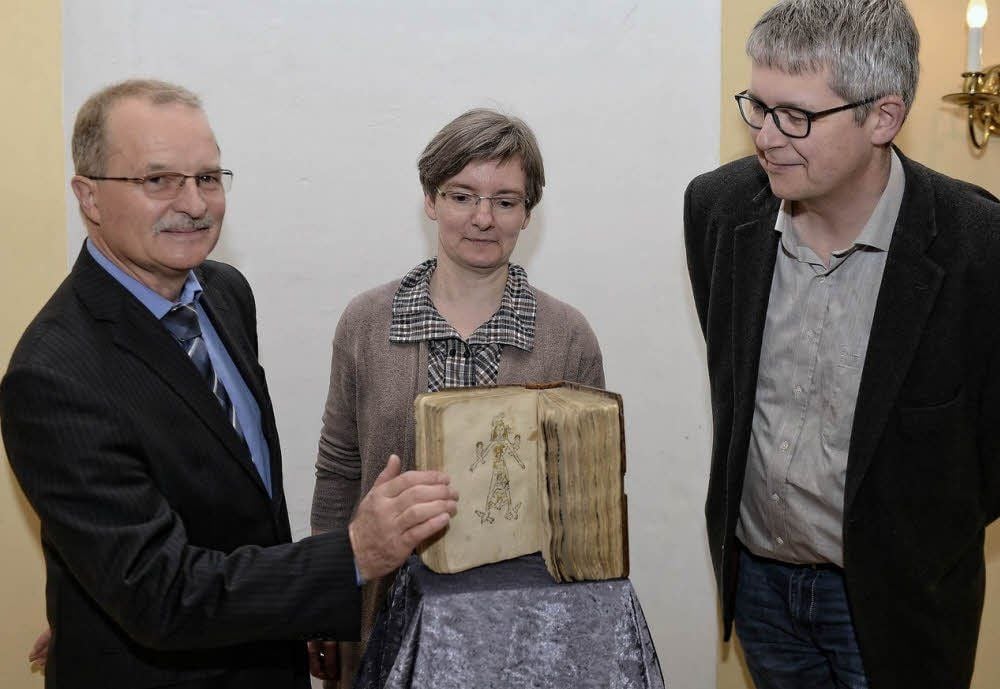 Werner Lautenschläger, Vorstandsvorsitzender Wohnungsverein Dessau (l.) und Martine Kreißler, Leiterin der Wissenschaftlichen Bibliothek geben das wertvolle Buch in die Hände von Christoph Roth, Buchsanierung Leipzig.