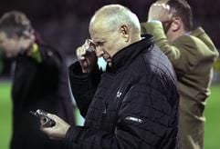 Der Cottbuser Präsident Dieter Krein hält am 1. April 2005 im Erzgebirgsstadion in Aue (Sachsen) während eines Telefonats ein Teil des Feuerwerkskörpers in der Hand, der den Cottbuser Trainer Petrik Sander verletzt hatte. (Foto: dpa)