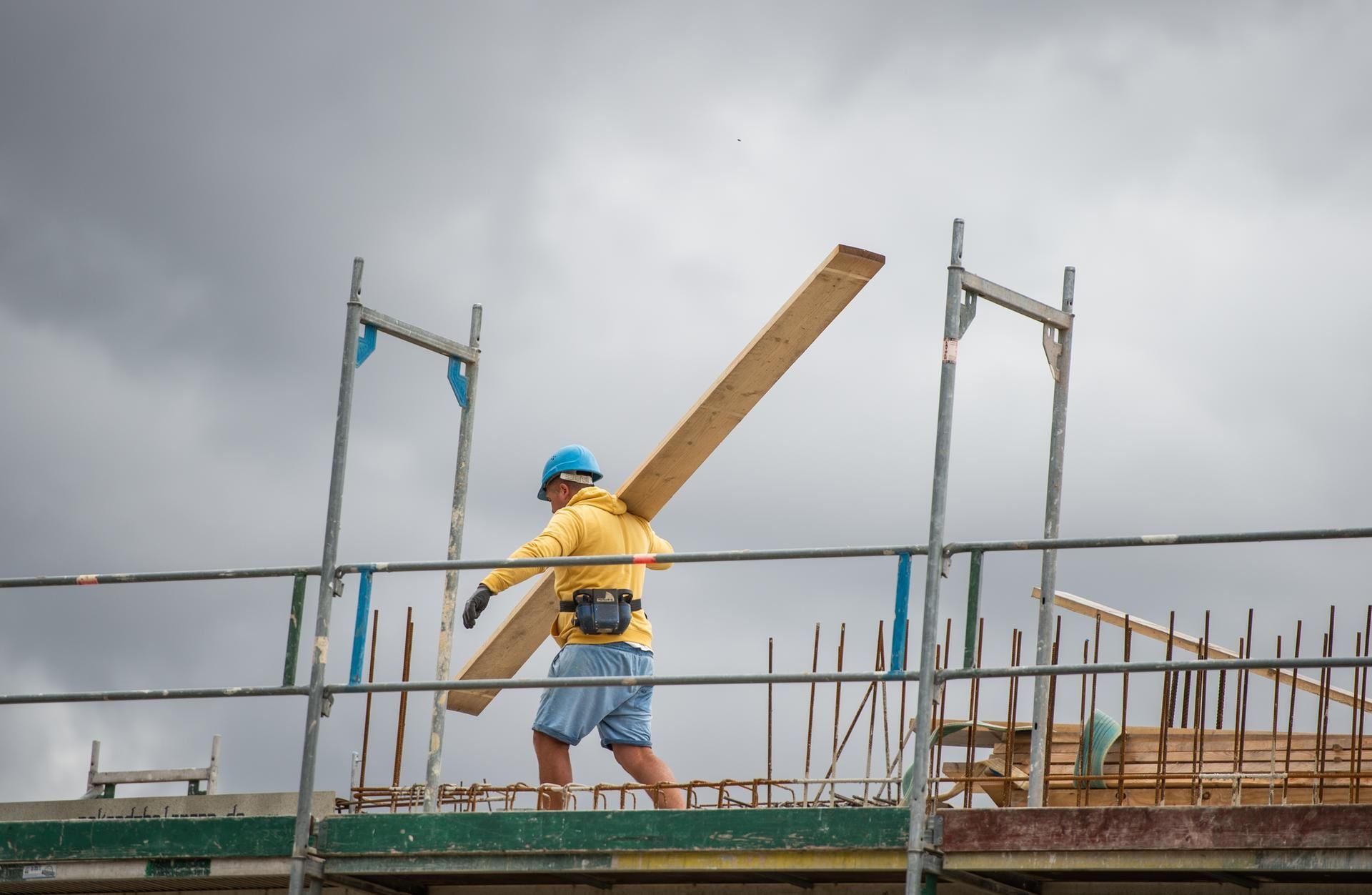 Ein Bauarbeiter trägt auf einer Baustelle auf einem Hausdach ein Brett. (Symbolbild)