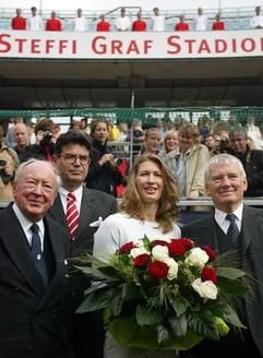 Lachend steht die ehemalige Tennisspielerin Steffi Graf am Samstasg (25. September 2004) auf dem Centercourt der Tennisanlage Rot-Weiss, die während einer Zeremonie in «Steffi Graf Stadion» umbenannt wurde. Links steht der Ehrenpräsident des Vereins, Wolfgang Hofer und rechts Bundesinnenminister Otto Schily, links neben Steffi Graf der Präsident des Tennisvereins, Hans Jürgen Jobsky. (Foto: dpa)