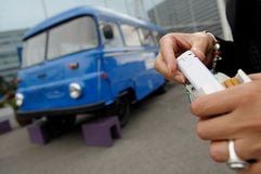 Eine Mitarbeiterin des Hotels Park Inn in Berlin hält vor dem «Vier-Sterne-Raucherbus» eine Packung Zigaretten und ein Feuerzeug in den Händen. (Foto: dpa)