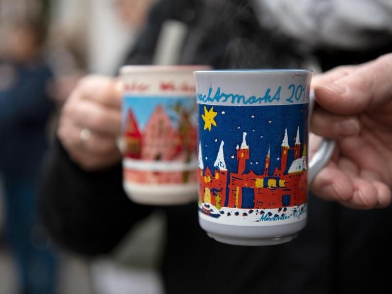 Besucher auf dem Lübecker Weihnachtsmarkt auf dem Rathausmarkt halten Keramikbecher, die mit Punsch gefüllt sind. Foto: Rainer Jensen/Archiv