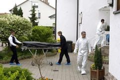Eine Leiche wird auf einer Bahre aus dem Haus gefahren, daneben Beamte der Spurensicherung. (Foto: dpa)