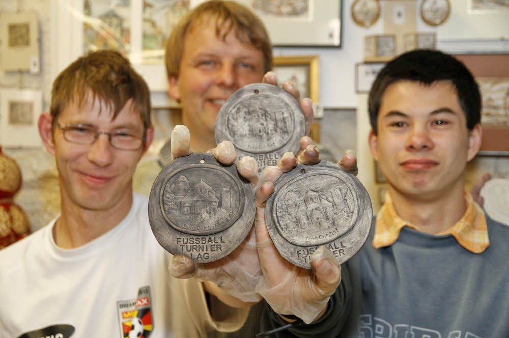 Der Geschäftsführer der Heilpädagogischen Hilfe, Sören Lorenz (M.), präsentiert mit den Spielern Klaus-Dieter (l.) und Jens die Medaillen.