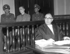 Heinrich Pommerenke (2.v.l) sitzt zwischen zwei Polizisten auf der Anklagebank im Schwurgerichtssaal in Freiburg, vorne sitzt sein Verteidiger (Archivfoto vom 03.10.1960). (Foto: dpa)