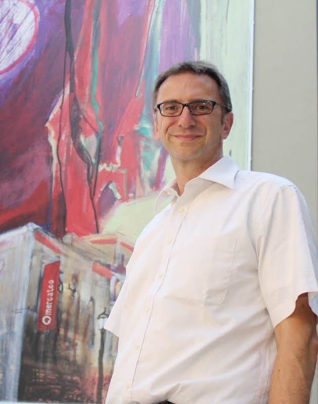 Firmenchef Peter Ledermann steht in Köthen vor einem meterhohen Bild am Unternehmensstandort in der Museumsgasse. Darauf ist der Firmensitz und die St.-Jakobs-Kirche gezeichnet.