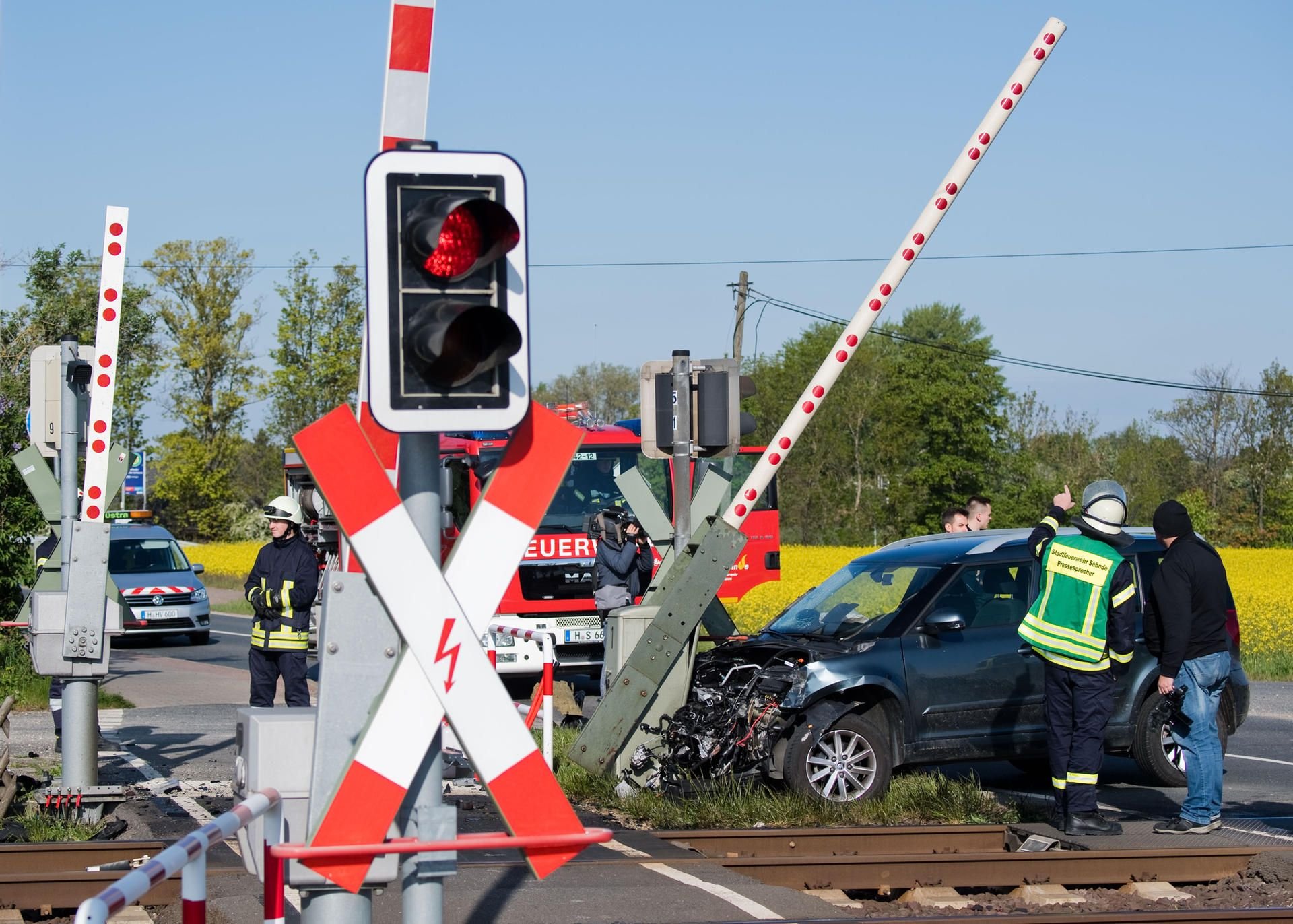 Ein beschädigter Pkw klemmt unter einer Bahnschranke. Feuerwehrleute sichern die Unfallstelle in Sehnde.