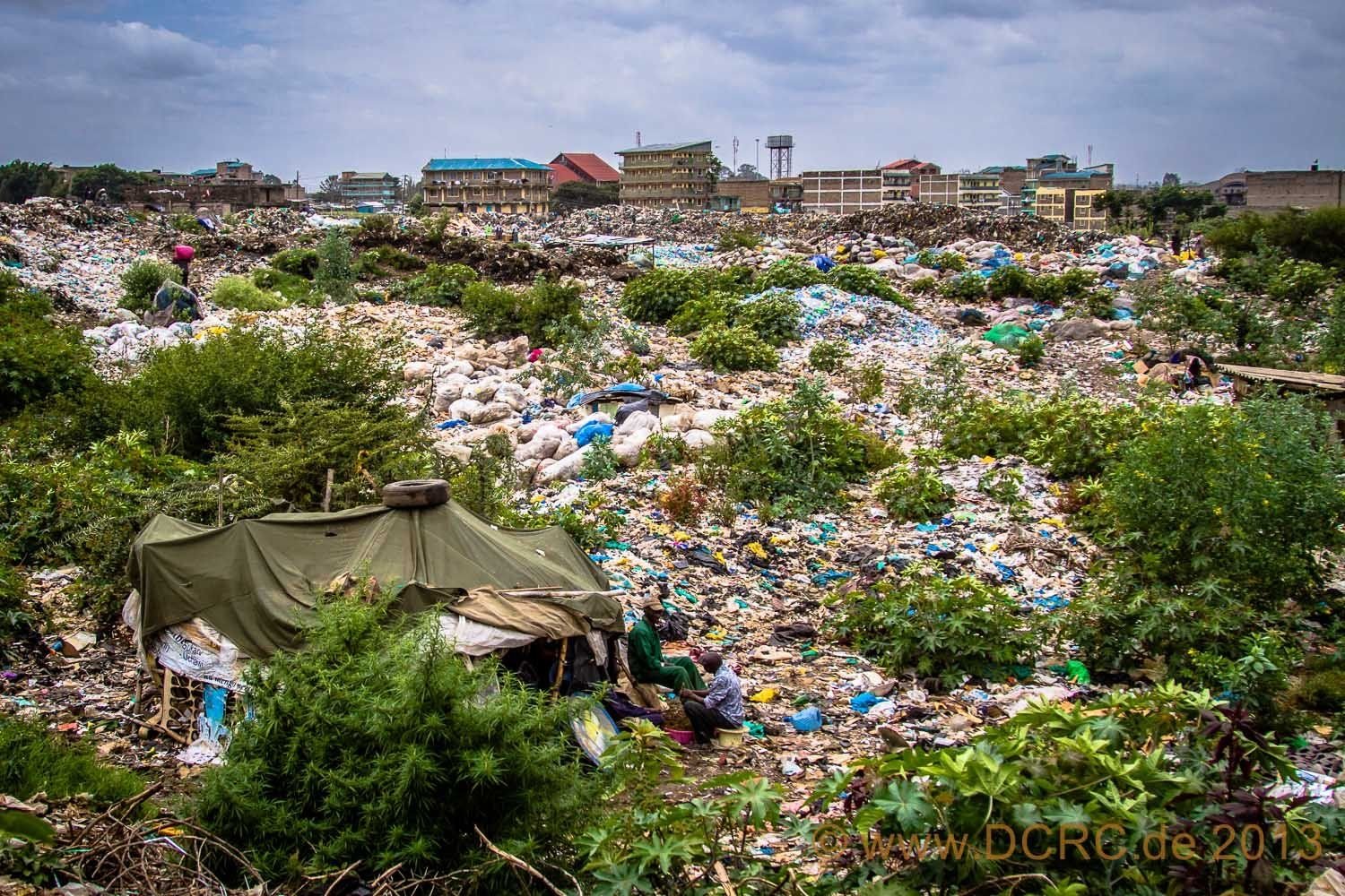 Neben dem PET-Flaschenfeld liegt in einer Senke eine kleine Hütte, die aus Holzstangen und Plastikplanen errichtet ist.
