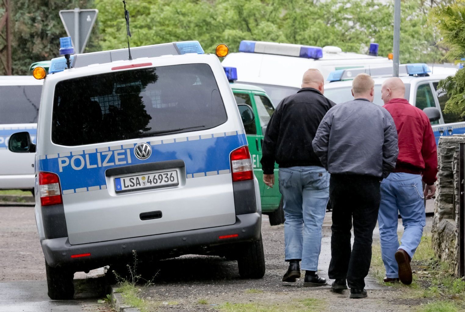 Junge Männer mit kurz geschorenen Haaren und Springerstiefeln gehen in Nienhagen (Sachsen-Anhalt) an Polizeifahrzeugen vorbei zu einem Rechtsrockkonzert.