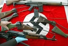 Ein Polizeibeamter legt am Donnerstag (28.04.2005) im Polizeipräsidium Augsburg automatische Waffen auf eine Hackenkreuzfahne. (Foto: dpa)