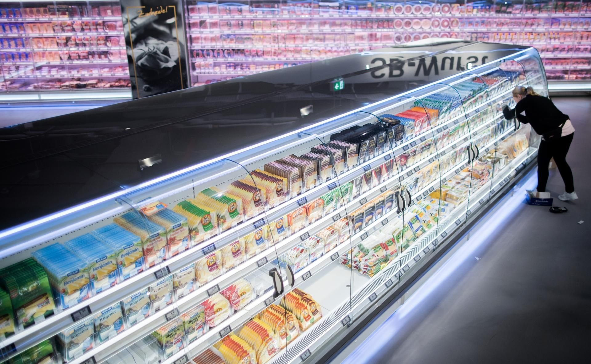 Frau bedient sich an der Käsetheke eines Supermarktes.