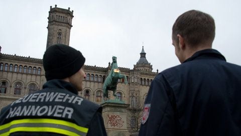 Feuerwehrmänner stehen vor dem Hauptgebäude der Leibniz Universität in Hannover und betrachten einen goldenen Leibniz-Keks an dem Niedersachsenpferd. (FOTO: DPA)