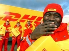 Der Paketzusteller Eduardo aus Angola versucht am Montag (02.02.2004) in Berlin in seiner Rolle als Model bei der Vorstellung der neuen Unternehmenskleidung der DHL ein Lachen zu unterdrücken, im Hintergrund Jeronimo aus Deutschland, Hakan und Serhat aus der Türkei. (Foto: dpa)
