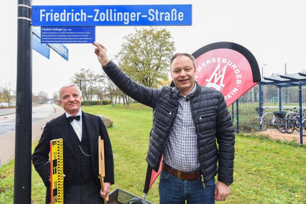 Michael Hayn bringt das Zusatzschild an, für das er die Patenschaft übernommen hat. Der als Friedrich Zollinger verkleidete Merseburger Kulturamtschef Michael George schaut ihm dabei ganz genau auf die Finger.
