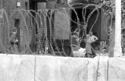 Eine Familie hinter Stacheldraht bewacht von Volkspolizisten der DDR während der Zwangsräumung von Häusern in der Bernauer Straße in Berlin, 1961. Nachdem bereits die nach Westberlin gehende Türen und Parterre-Fenster zugemauert wurden, entdeckten Fotografen kurz darauf auch mit Stacheldraht versehene Fenster. (FOTO: ARCHIV/DPA)
