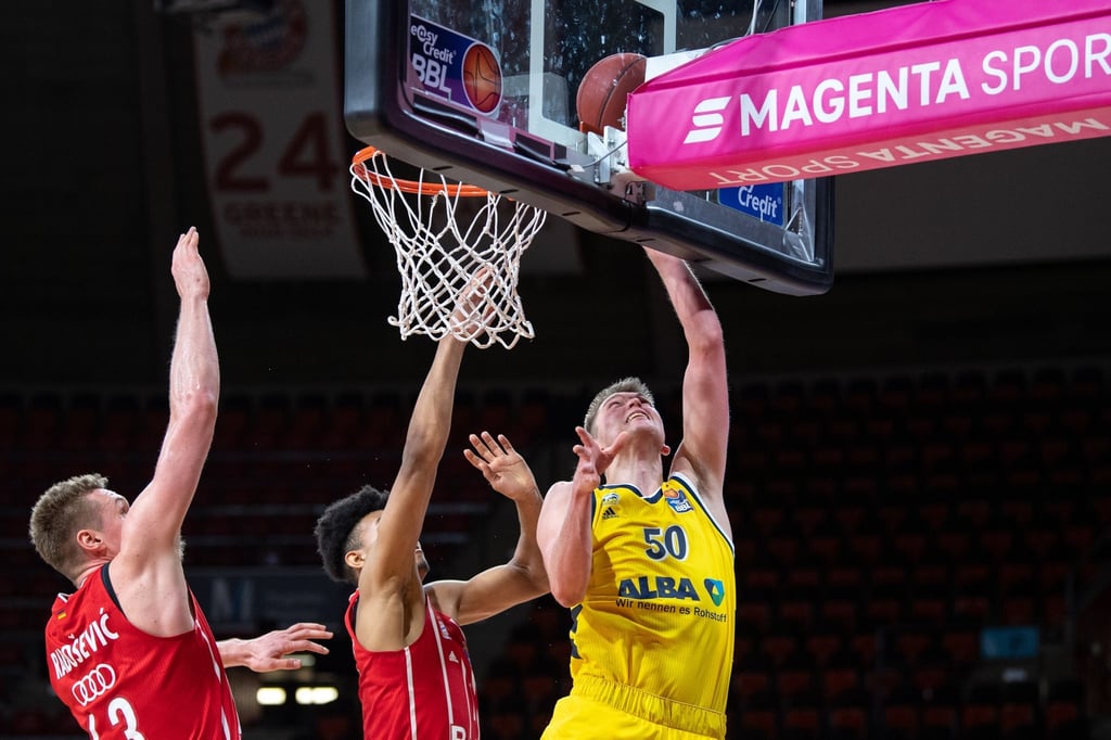 Leon Radosevic (l-r) und Jason George von Bayern München versucht Ben Lammers von Alba Berlin am Korb zu blocken.