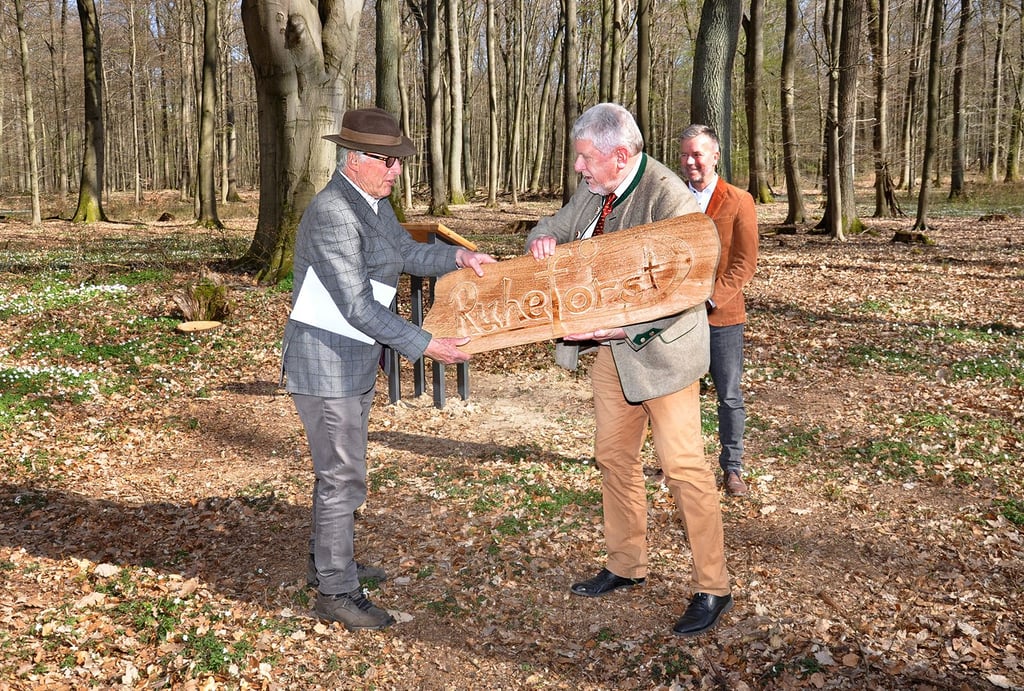 Andreas Graf von Bernstorff (links) nimmt von Jost Arnold als Präsent ein ?Ruheforst?-Schild entgegen. Bürgermeister Nico Schulz (im Hintergrund) beobachtet die Szene.