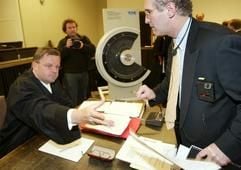 Ein Schriftstück des US-Anwalts Edward Fagan (r) wirft Verteidiger Otmar Kury, der einen der Bahn-Ingenieure vertritt, am Mittwoch (15.01.2003) im Landgericht in Hannover vor der Fortsetzung des Prozesses um die ICE-Katastrophe von Eschede mit 101 Toten ungelesen über den Tisch. Im Hintergrund steht ein 1:1 Schnittmodell eines ICE-Radreifens. Internationale Gutachter beginnen am Mittwoch (15.01.) zur Ursache des Radreifenbruchs auszusagen. Die Strafkammer will von den Gutachtern wissen, ob der Radreifen nach dem Stand der Technik richtig konstruiert und dimensioniert war und ob er so lange hätte genutzt werden dürfen. Im Prozess müssen sich drei Ingenieure wegen fahrlässiger Tötung und Körperverletzung verantworten. (Foto: dpa)
