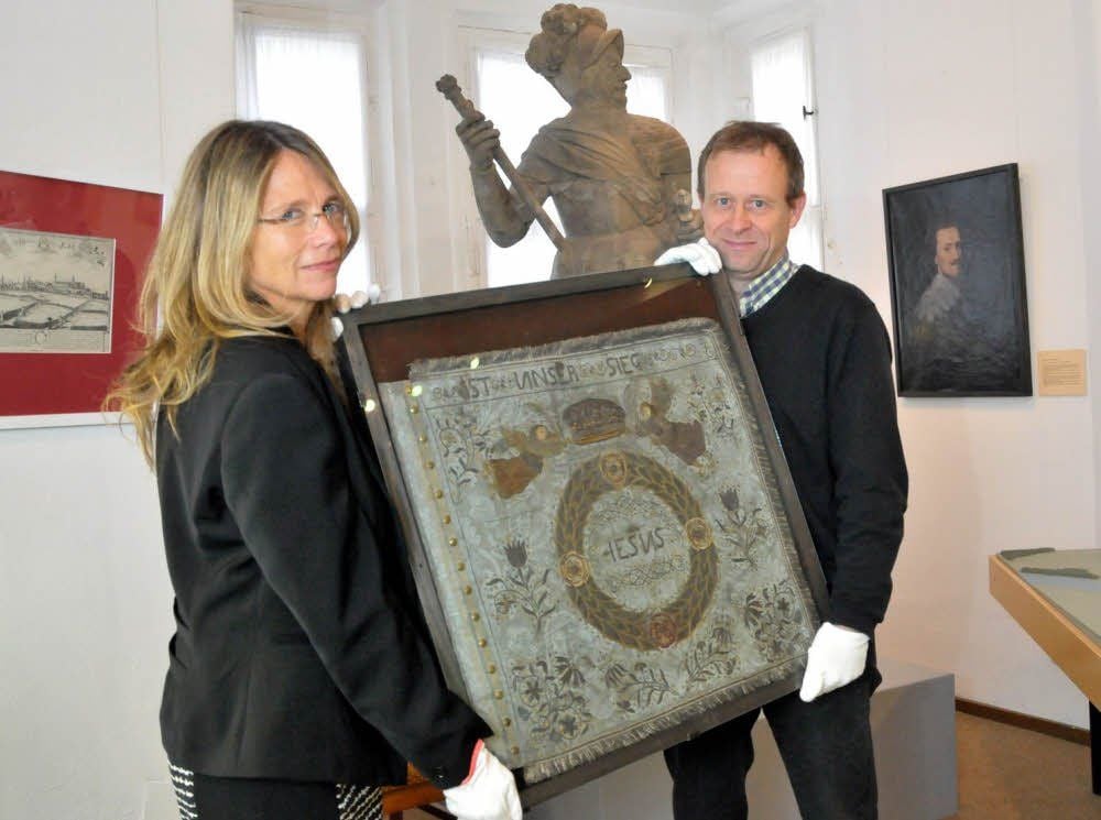 Bernburgs Museumsleiter Roland Wiermann übergibt die Standarte aus dem 17. Jahrhundert an Urte Dally vom Landesmuseum für Vorgeschichte in Halle. Dort wird die spezielle Flagge ab 6. November im Rahmen der Ausstellung „Krieg. Eine archäologische Spurensuche“ zu sehen sein.