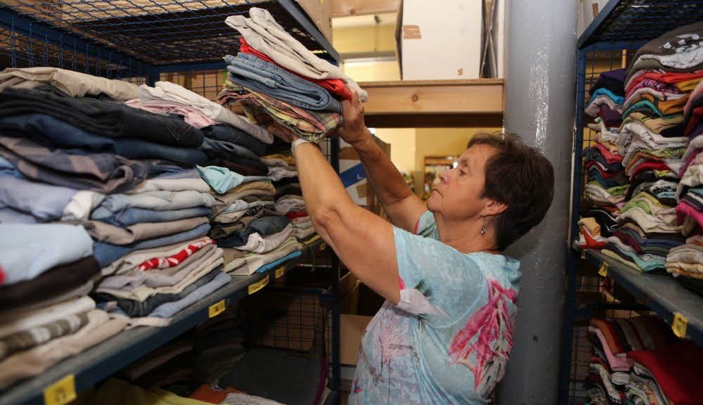 Eine Mitarbeiterin sortiert Kleidungsstücke in die Regale einer Kleiderkammer