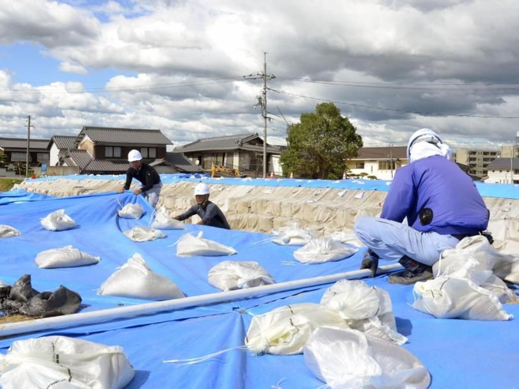 Arbeiter legen Sandsäcke über blaue Planen in Vorbereitung auf den herannahenden Taifun. Foto: Kyodo News/AP