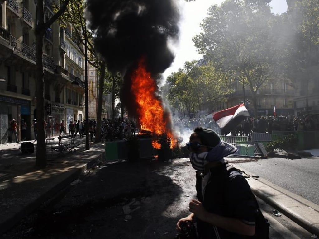 Ein vermummter Protestler geht an einer brennenden Barrikade vorbei. Foto: Thibault Camus/AP
