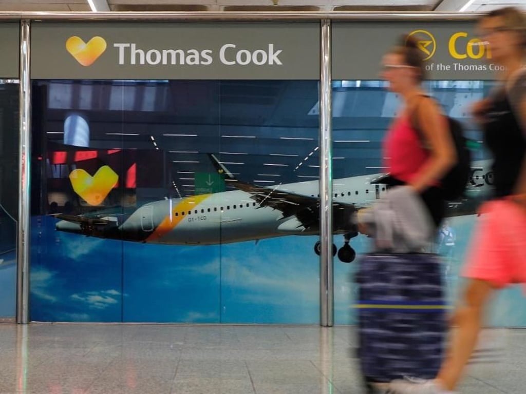 Passagiere neben einem großen Werbeschild von Thomas Cook am Flughafen von Palma de Mallorca. Foto: Clara Margais