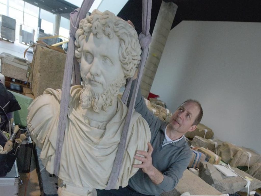 Restaurator Gunther Weinreuter hebt im Limesmuseum die Statue des römischen Kaisers Septimius Severus, daneben liegt eine Büste des Kaiser Caracalla. Foto: Stefan Puchner