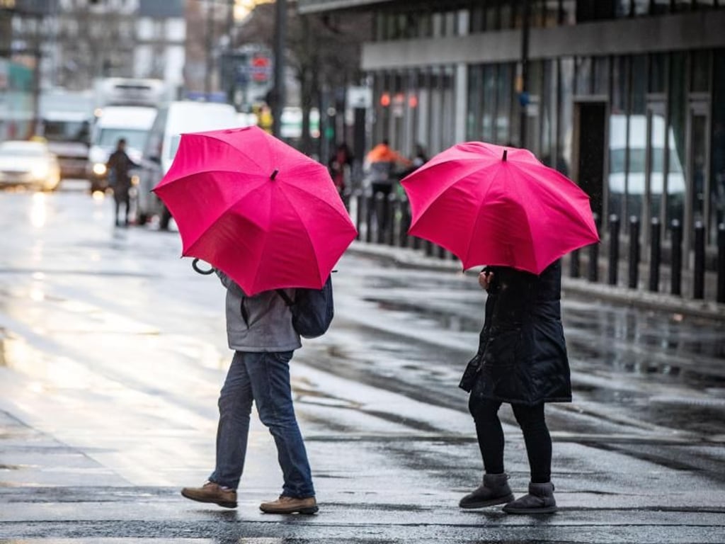 Kleiner Farbtupfer: Passanten mit Regenschirmen überqueren bei Wind und Regen eine Kreuzung in der Frankfurter Innenstadt. Foto: Frank Rumpenhorst