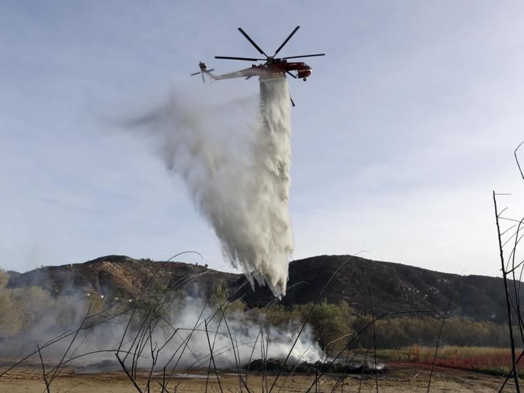 Ein Löschhubschrauber wirft seine Wasserladung über einem Schwelbrand von Holzschnitzeln und Mulch ab. Foto: Gregory Bull