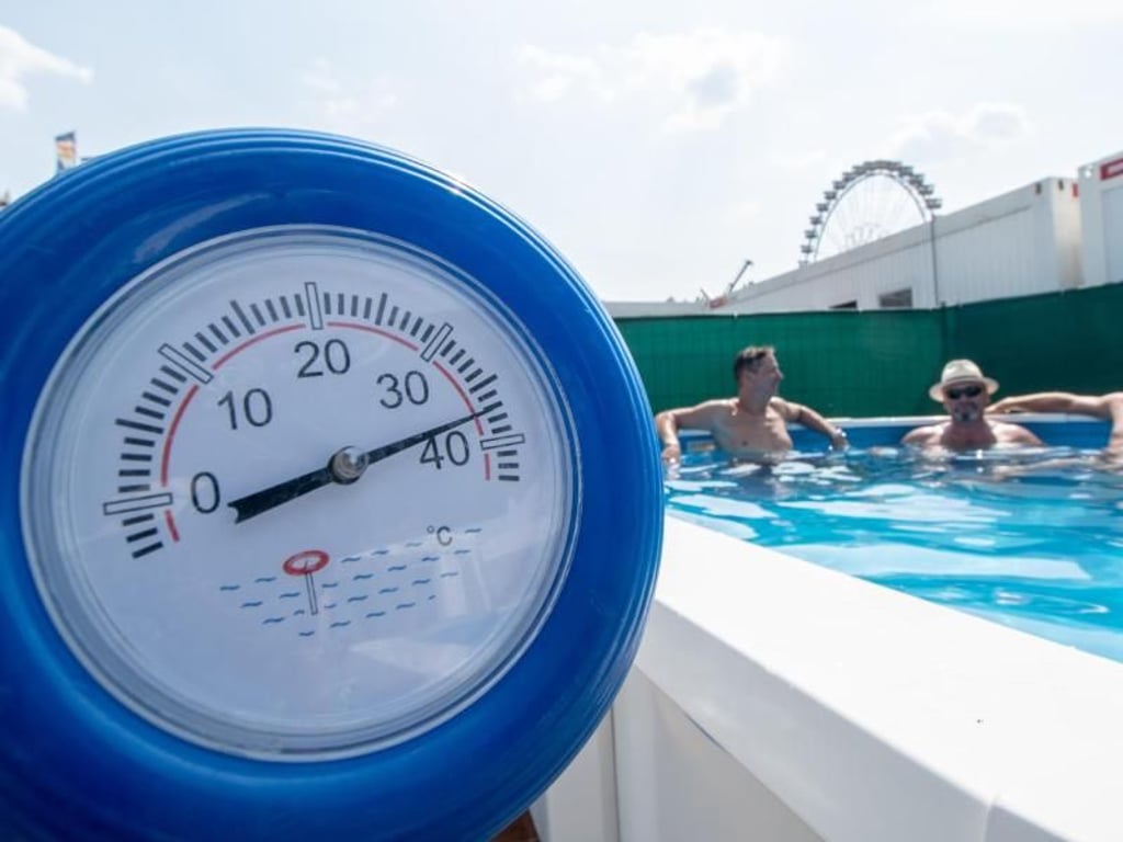 Im bayerischen Straubing zeigt ein Thermometer schon 38 Grad an, während sich die Monteure eines Messestands für Pools während einer Pause auf dem Gelände der Ostbayernschau abkühlen. Foto: Armin Weigel
