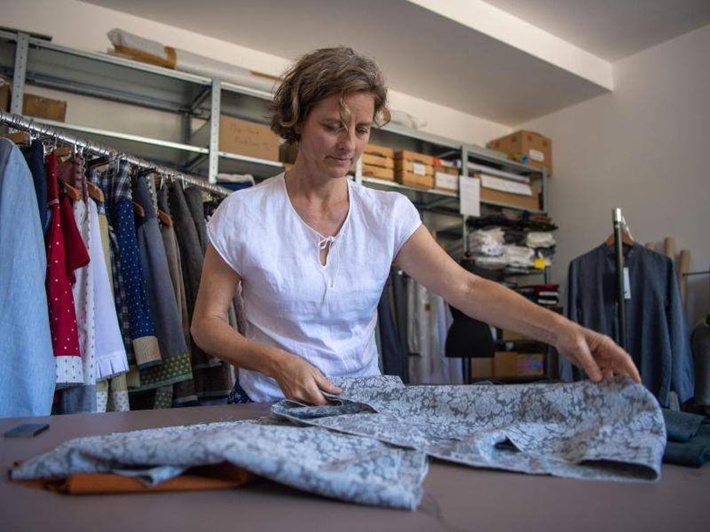 Caroline Herrmann-Lauenstein, Mode-Designerin, kombiniert auf einem Tisch in einer Werkstatt ihrer Manufaktur verschiedene Stoffe zu einem Design. Foto: Lino Mirgeler/dpa