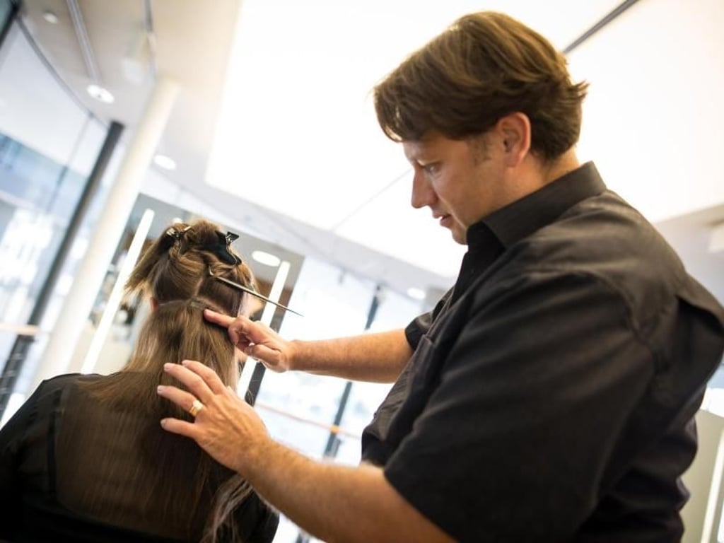 Mit flachen Tapes können die Extensions zwischen das eigene Haar geklebt werden. Hier arbeitet Friseurmeister Marcus Hertel einer Kunden Extensions ein. Foto: Christoph Schmidt