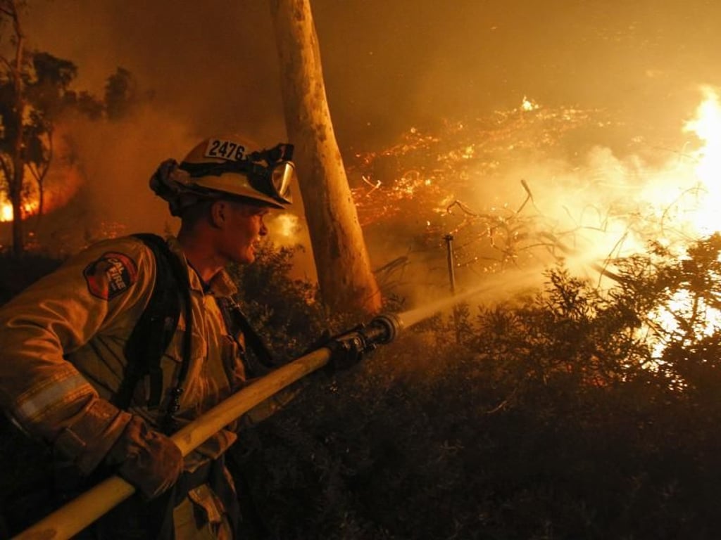 Ein Feuerwehrmann löscht bei San Diego einen Buschbrand an einem Hügel hinter den Geschäften des River Village Einkaufszentrums. Foto: Hayne Palmour Iv/San Diego Union-Tribune via ZUMA