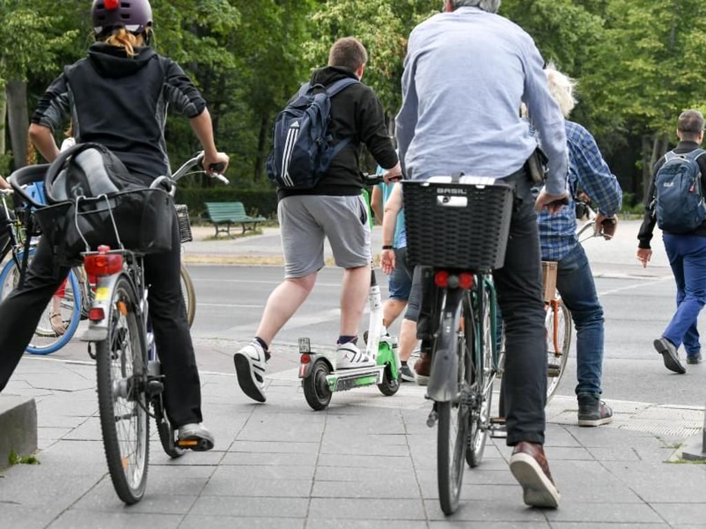 Ein E-Tretroller zwischen Fahrrädern und Autos im Straßenverkehr. Foto: Jens Kalaene