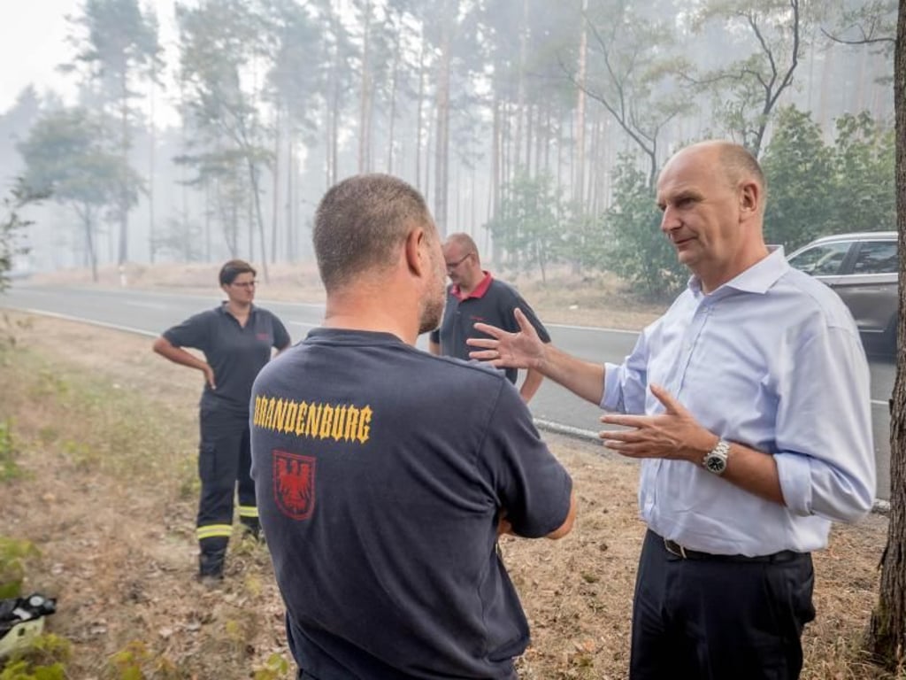 Dietmar Woidke, Ministerpräsident von Brandenburg, spricht mit Feuerwehrleuten im Wald. Foto: Michael Kappeler
