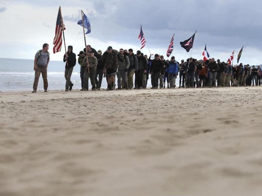 Männer gehen mit Flaggen der alliierten Truppen den Omaha-Beach in der Normandie entlang. Foto: David Vincent/AP