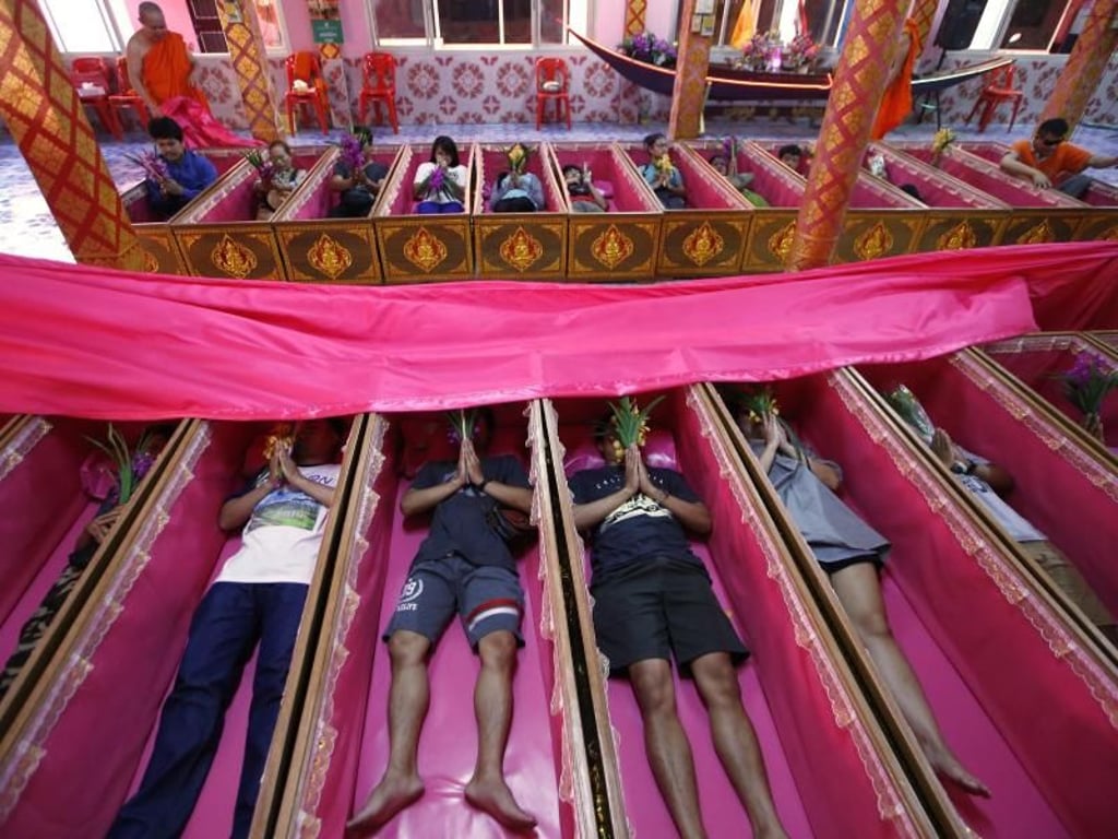 Gläubige liegen in rosa Särgen und beten während einer Zeremonie, die Tod und Wiedergeburt symbolisiert - und von Unglück befreit. Foto: Sakchai Lalit/AP