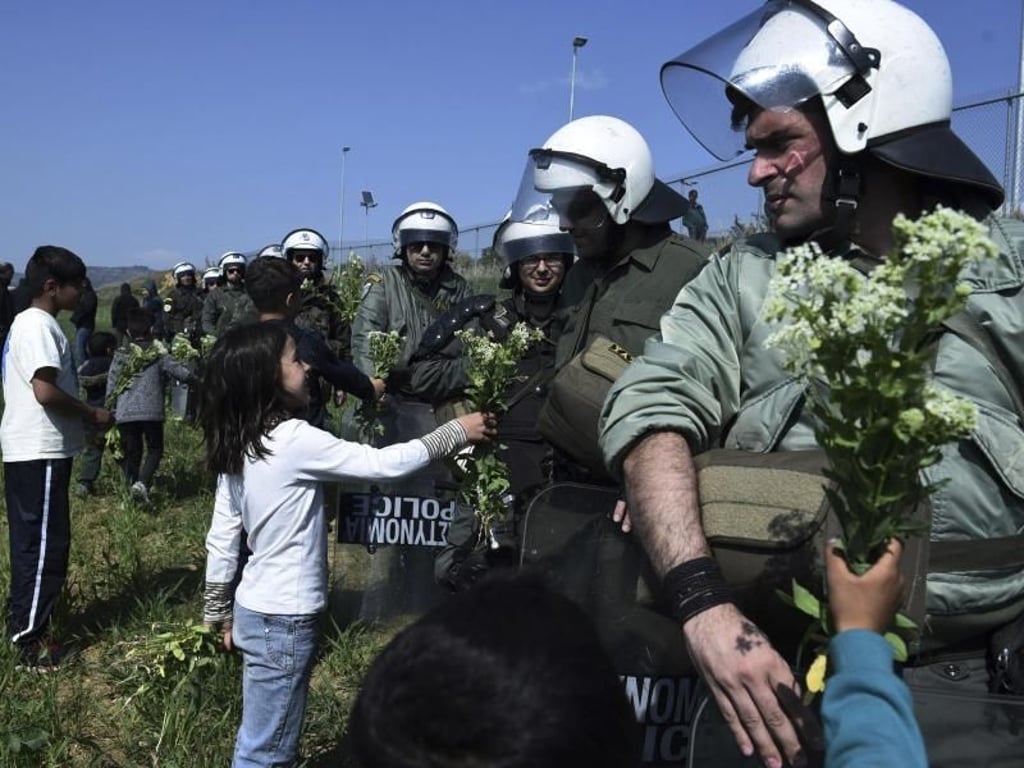 Kinder von Migranten bieten Bereitschaftspolizisten Blumen am Zaun eines Flüchtlingslagers an. Foto: Giannis Papanikos/AP