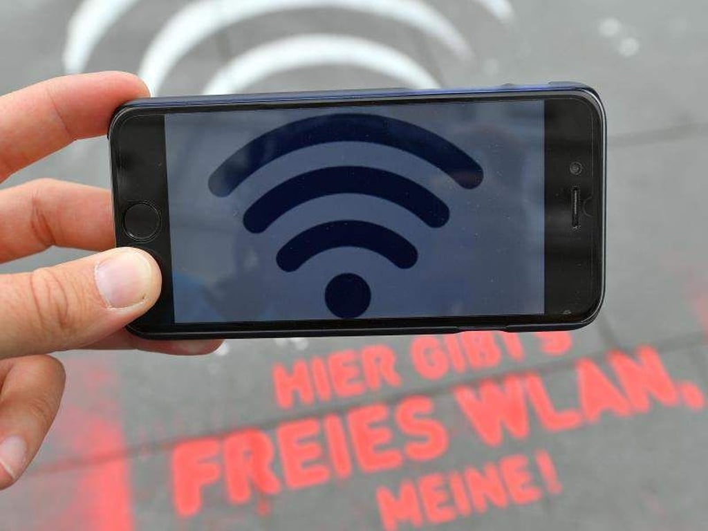 WLAN-Symbol auf Handy über Schriftzug «Hier gibt's freies WLAN». Foto: Hendrik Schmidt/Archiv