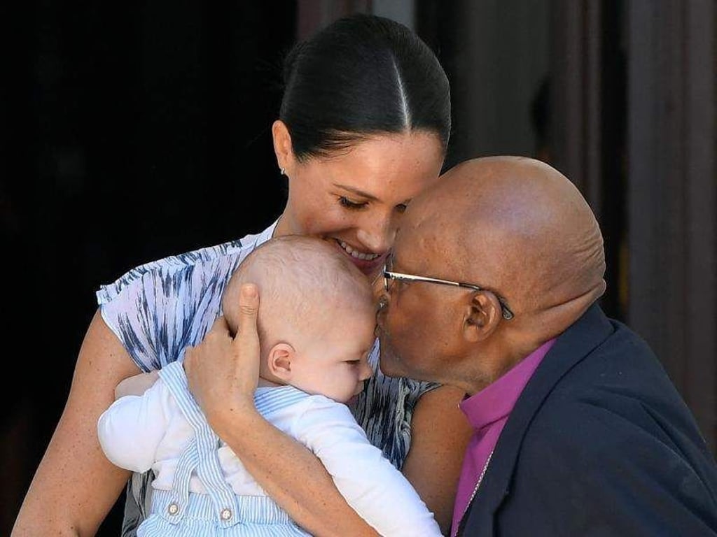 Der kleine Archie wird von Desmond Tutu mit einem Kuss begrüßt. Und Meghan strahlt über das ganze Gesicht. Foto: Toby Melville/PA Wire