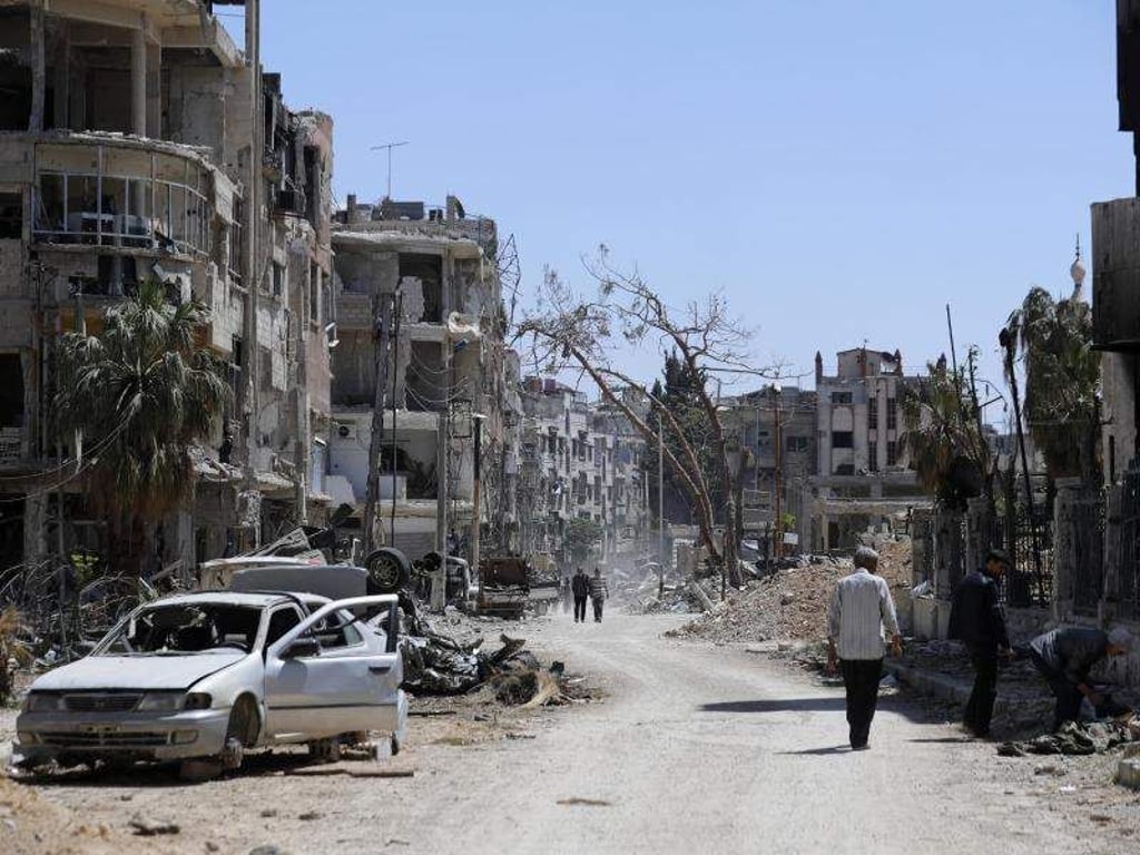 Menschen gehen an zerstörten Häusern und Autos im syrischen Duma vorbei. Foto: Hassan Ammar/AP