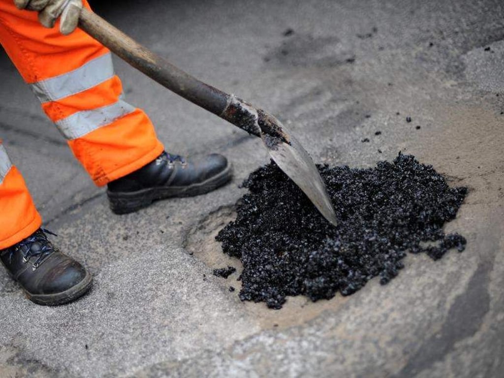 Ein Arbeiter füllt ein Schlagloch mit Asphalt. Foto: Uwe Zucchi/Archiv