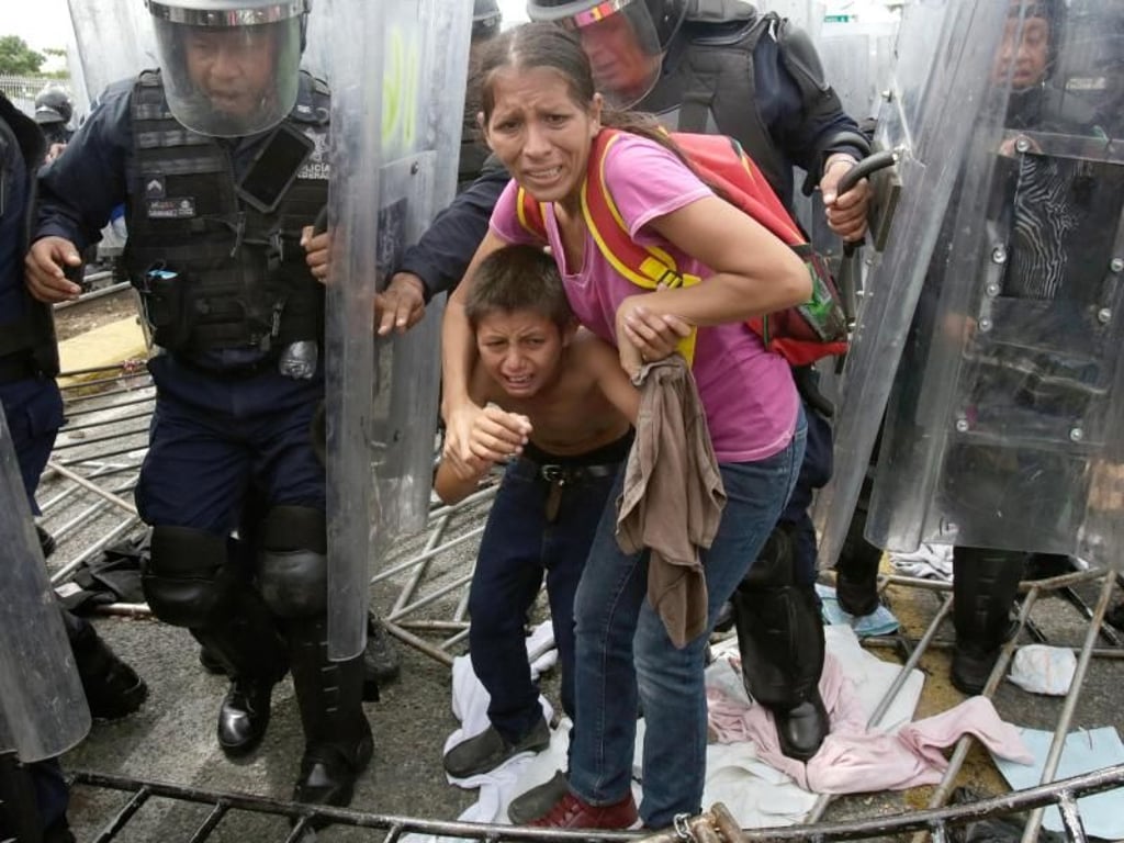 Eine Migrantin und ihr Kind werden von der mexikanischen Bundespolizei vor Steinen geschützt, die von Unbekannten am Grenzübergang in Ciudad Hidalgo geworfen werden. Foto: Moises Castillo/AP