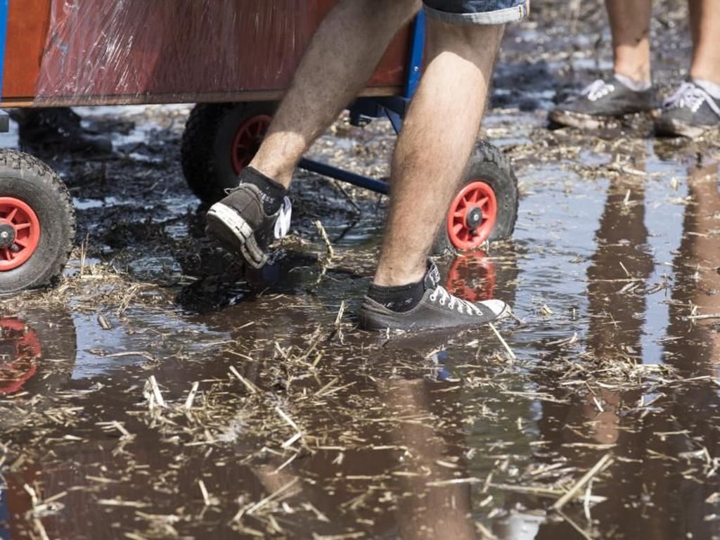Die ersten Besucher des Hurricane Festivals in Scheeßel (Niedersachsen) laufen durch Pfützen auf das Gelände. Foto: Jörg Sarbach