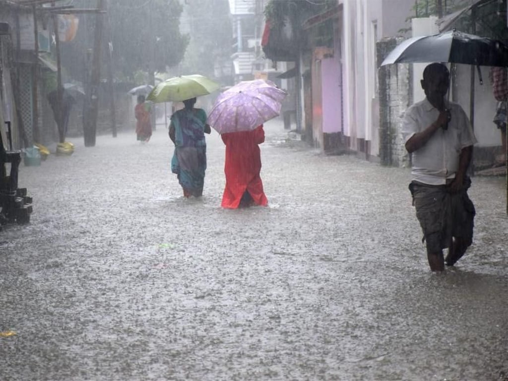 Menschen mit Regenschirmen waten indischen Balurghat durch eine überflutete Straße. Foto: Balurghat-Majidur Sardar