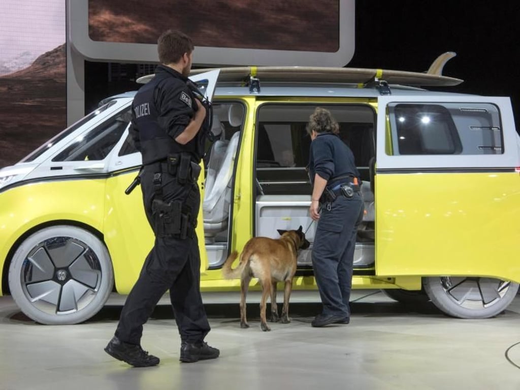 Mit einem Sprengstoffspürhund untersuchen Polizisten kurz vor der Ankunft von Bundeskanzlerin Merkel Fahrzeuge auf der IAA, hier einen ID Buzz von Volkswagen. Foto: Boris Roessler